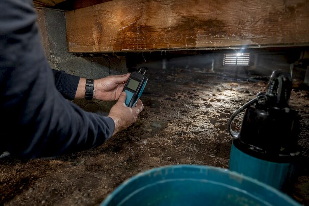 Hands measuring moisture in crawl space wood
