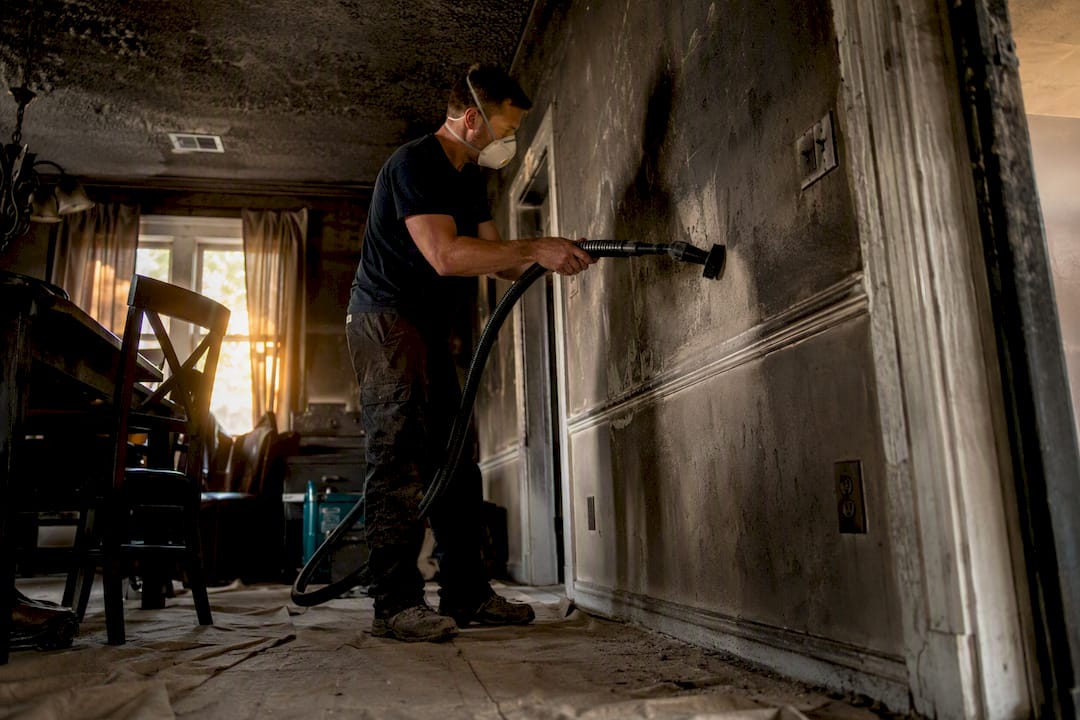 Technician vacuuming soot from fire-damaged home wall